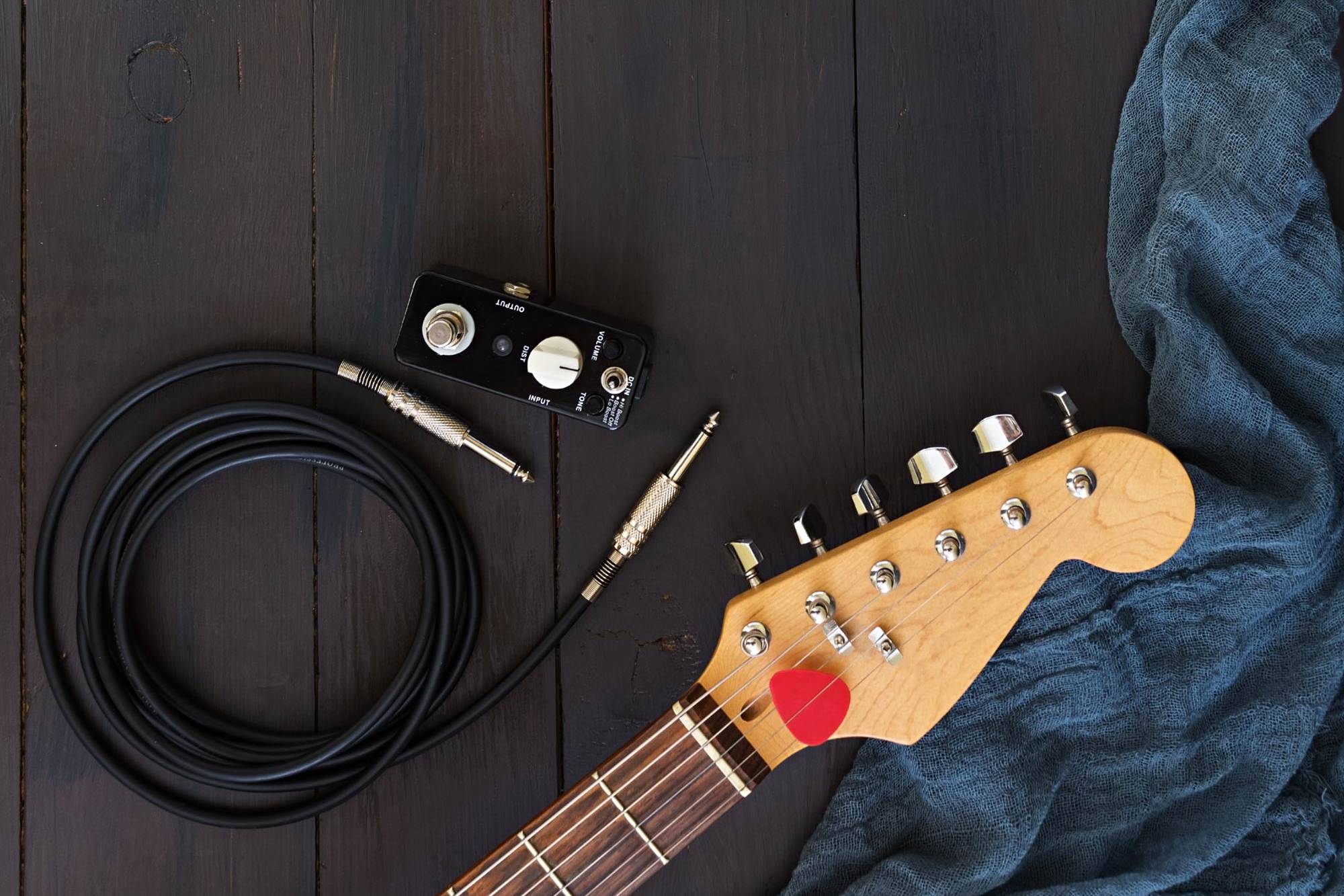 An electric guitar neck, a coiled lead, and a towel laid out on a wooden floor
