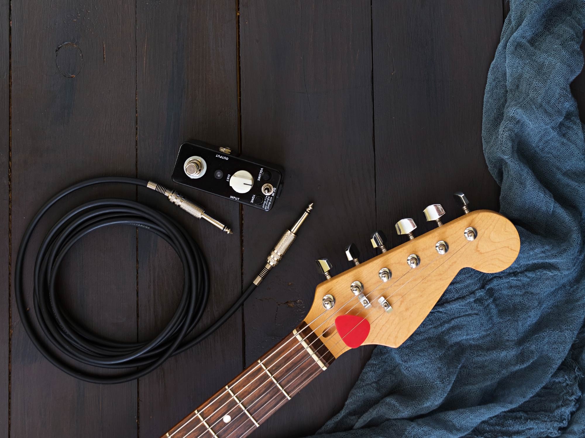 An electric guitar neck, a coiled lead, and a towel laid out on a wooden floor